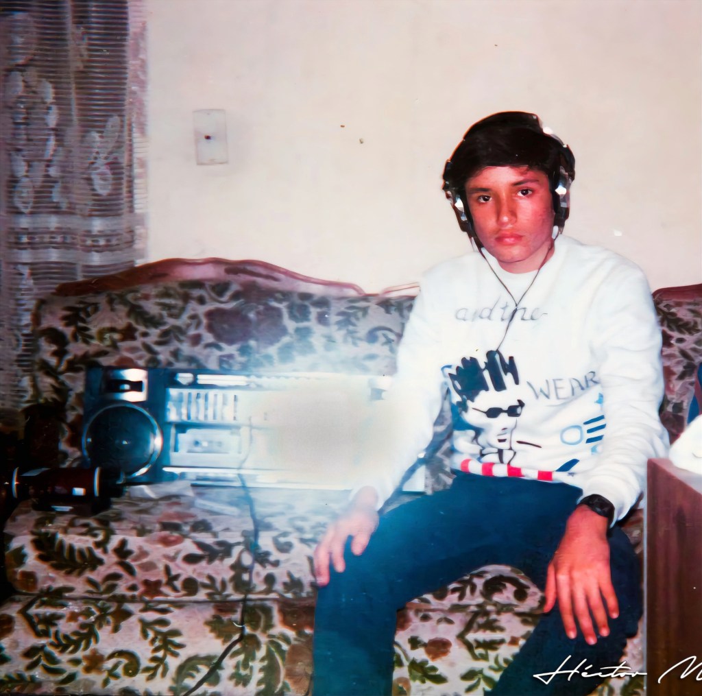 Héctor de adolescente en 1987, sentado en un sillón floreado con audífonos puestos, junto a una grabadora de casetes